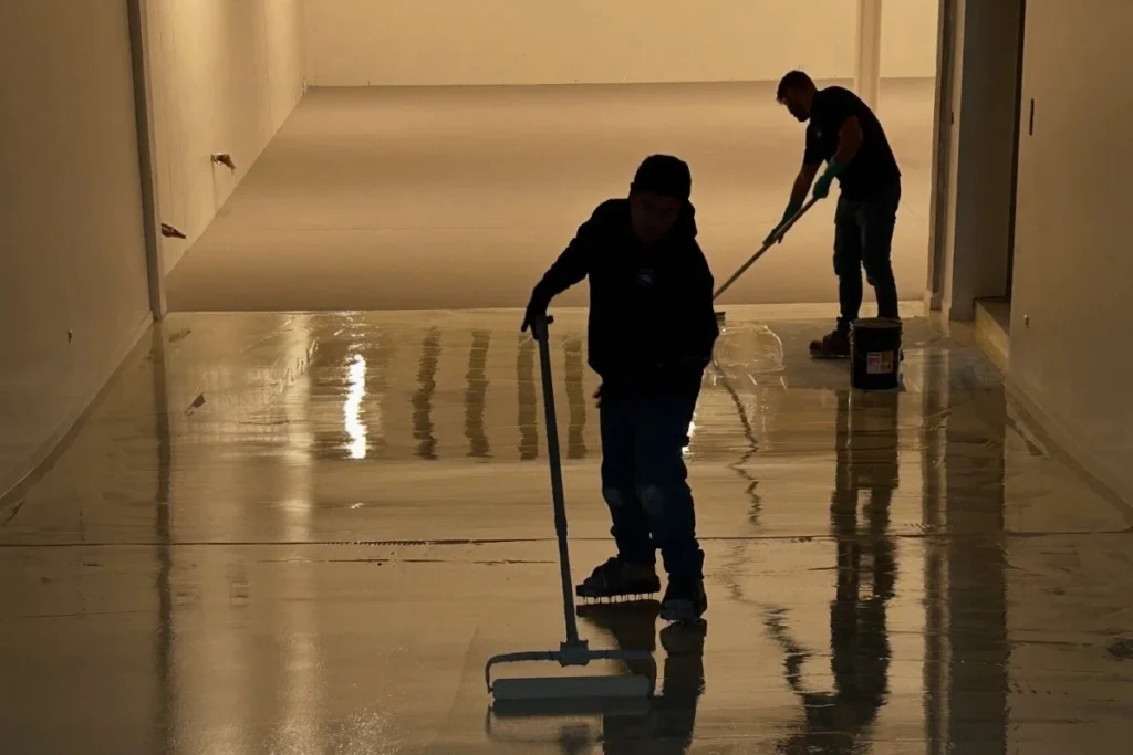 Two installers spreading epoxy coating on a garage floor with squeegees